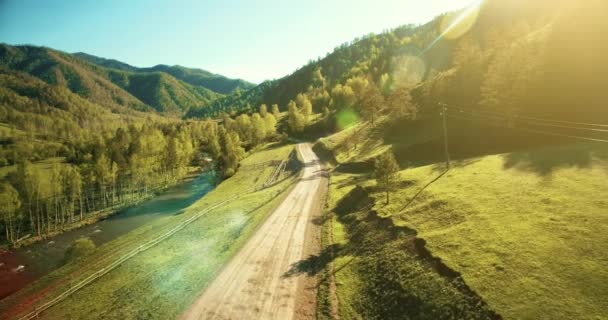4 k Uhd 空撮。山農村未舗装の道路と晴れた夏の朝に草原上低空気飛行。近くには緑の木々、太陽光線、山川 — ストック動画