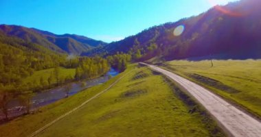 Güneşli yaz sabahında taze dağ nehri ve çayır üzerinde uçuşun ortasında. Aşağıdaki kırsal toprak yol.