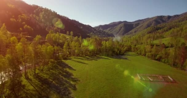 Vol en vol au-dessus d'une rivière de montagne fraîche et d'un pré au matin ensoleillé d'été. Chemin de terre rural en dessous. — Video