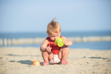 Denize yakın kumlu plajda oynayan Kırmızı elbiseli kız bebek.