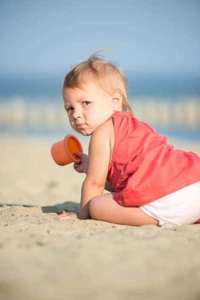Niña en vestido rojo jugando en la playa de arena cerca del mar . —  Fotos de Stock