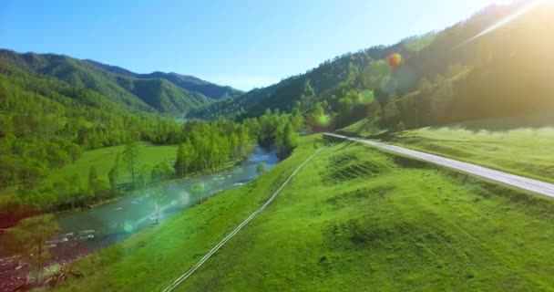 UHD 4K vista aérea. Vuelo bajo sobre el río fresco y frío de la montaña, prado y carretera en la soleada mañana de verano . — Vídeo de stock