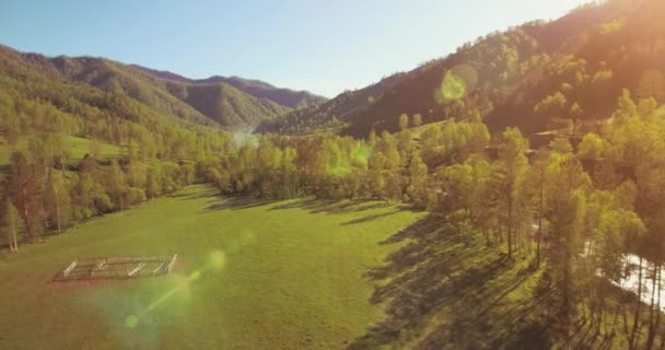 Mid air flight over fresh mountain river and meadow at sunny summer morning. Rural dirt road below. — Stock Video