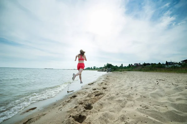 Giovane signora che corre alla soleggiata spiaggia di sabbia estiva. Allenati. Jogging — Foto Stock