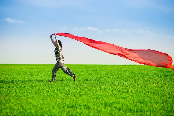 Beautiful young woman jumping on a green meadow with colored tissue — Stock Photo, Image