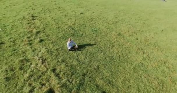 UHD 4k вигляд з повітря. Низький орбітальний політ над бізнесменом, що сидить на зеленій траві з блокнотом на полі — стокове відео