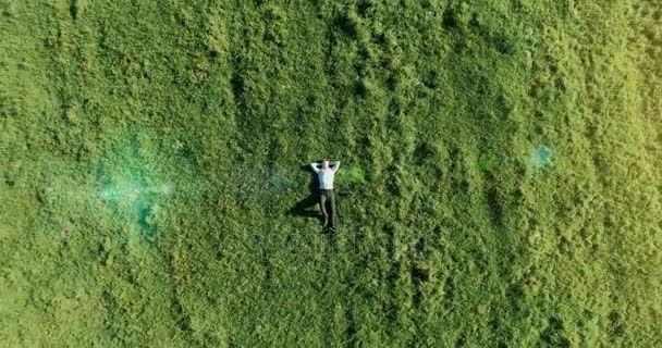 Вертикальный полет над бизнесменом, лежащим на свежем зеленом лугу. Вид сверху на расслабляющего человека . — стоковое видео