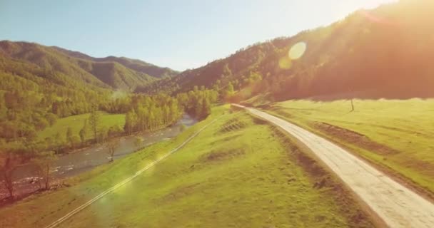 Vuelo en medio del aire sobre el río fresco de la montaña y el prado en la soleada mañana de verano. Camino de tierra rural abajo. — Vídeo de stock