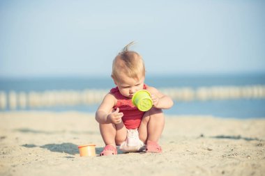 Denize yakın kumlu plajda oynayan Kırmızı elbiseli kız bebek.