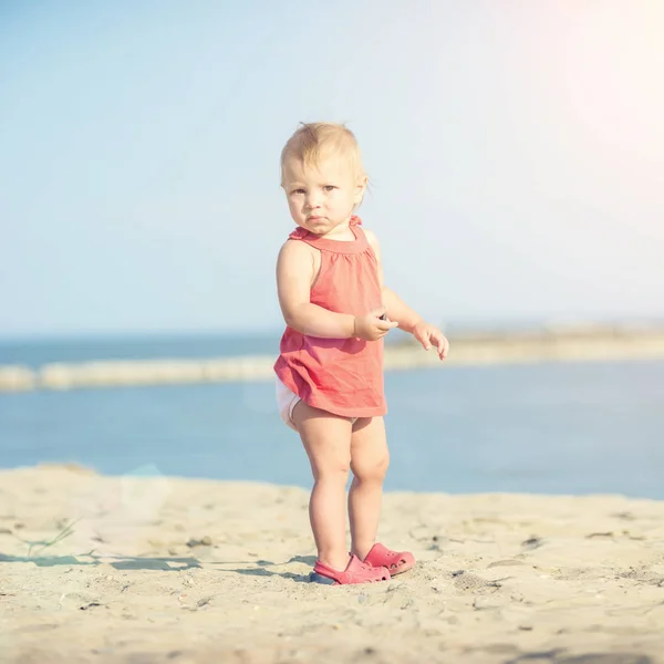 바다 근처의 모래 해변에 빨간 드레스에 여자 아기. — 스톡 사진