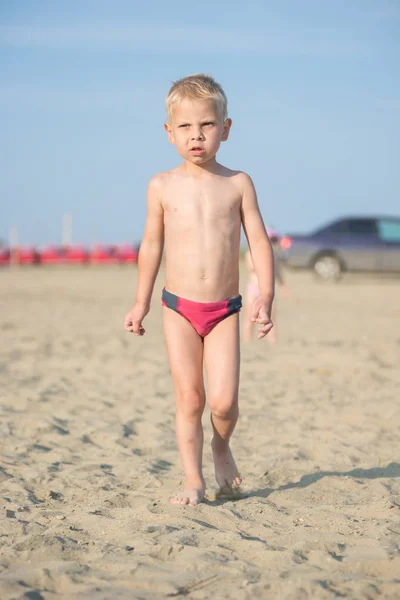 Carino il bambino che cammina sulla spiaggia sabbiosa vicino al mare. Costa oceanica . — Foto Stock