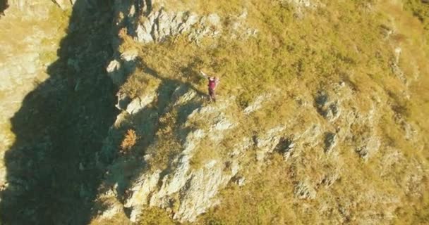 Voo radial orbital em torno do jovem caminhante em pé no topo do penhasco. Mãos para cima, vencedor. — Vídeo de Stock