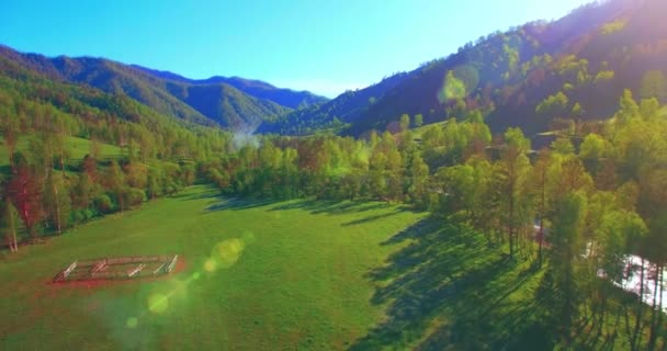 Vôo a meio do ar sobre o rio e o prado frescos da montanha na manhã ensolarada do verão. Estrada de terra rural abaixo. — Vídeo de Stock