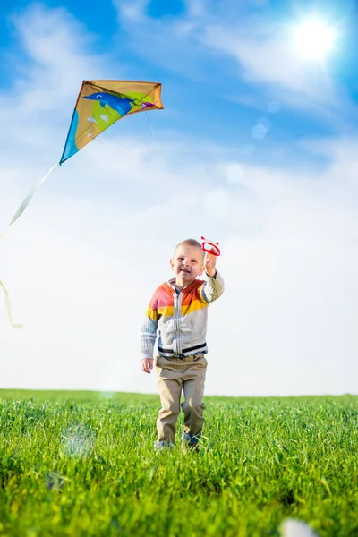 Jeune garçon jouant avec son cerf-volant dans un champ vert . — Photo