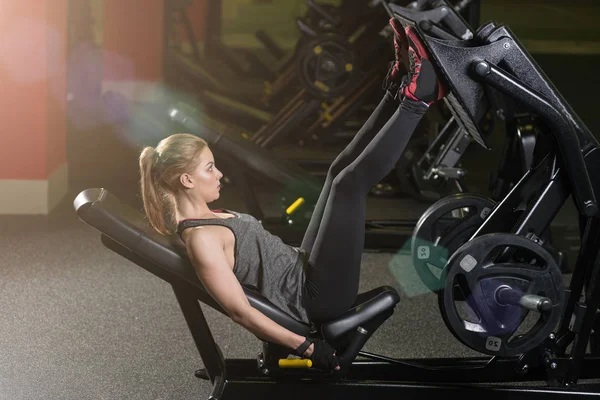 Sportieve vrouw met behulp van gewichten press machine voor de benen. Sportschool. — Stockfoto