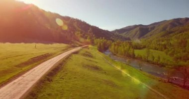 Güneşli yaz sabahında taze dağ nehri ve çayır üzerinde uçuşun ortasında. Aşağıdaki kırsal toprak yol.