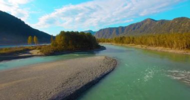 4k UHD hava görüntüsü. Güneşli yaz sabahında taze soğuk dağ nehri üzerinde alçak uçuş. Horisont 'ta yeşil ağaçlar ve güneş ışınları