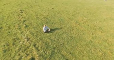 UHD 4k havadan görünümü. Defter pad ile yeşil çim sahasında oturan işadamı üzerinde düşük yörünge uçuş