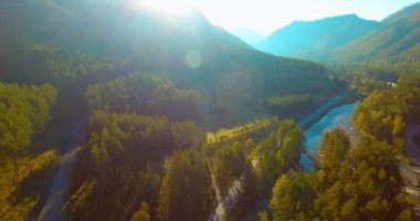 Güneşli yaz sabahında taze dağ nehri ve çayır üzerinde uçuşun ortasında. Aşağıdaki kırsal toprak yol.