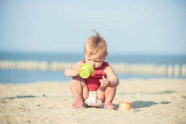 Denize yakın kumlu plajda oynayan Kırmızı elbiseli kız bebek.