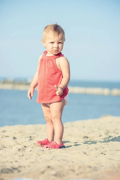 Niña en vestido rojo jugando en la playa de arena cerca del mar . —  Fotos de Stock