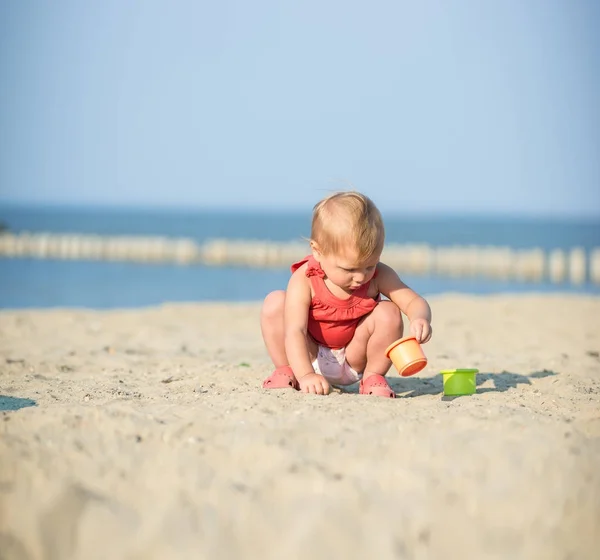 Девочка в красном платье играет на песчаном пляже у моря . — стоковое фото