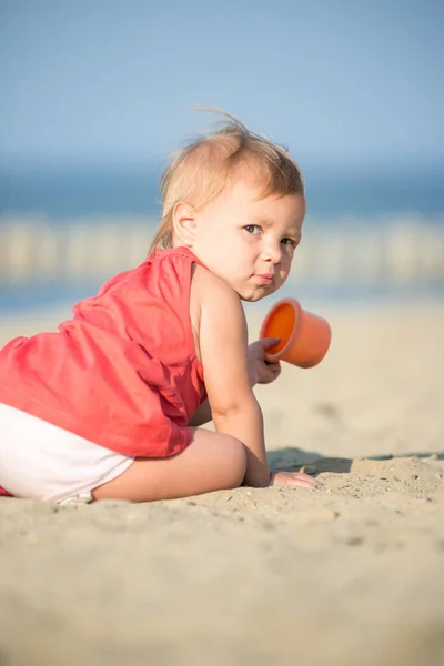 Mädchen im roten Kleid spielt am Sandstrand am Meer. — Stockfoto