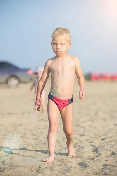 Ładny chłopczyk chodzenie na piaszczystej plaży w pobliżu morza. Na wybrzeżu Oceanu. — Zdjęcie stockowe