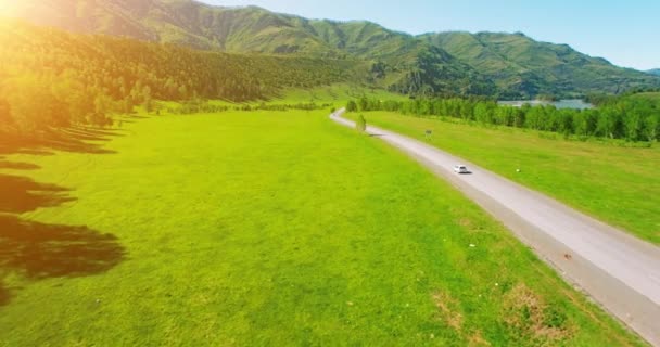 Vuelo sobre los coches en un camino sinuoso en las colinas y el prado. Carretera rural abajo . — Vídeos de Stock