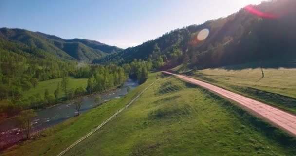 Mid air flygning över färska berg flod och äng på solig sommarmorgon. Landsbygdsvägen nedanför. — Stockvideo