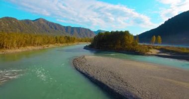 4k UHD hava görüntüsü. Güneşli yaz sabahında taze soğuk dağ nehri üzerinde alçak uçuş. Horisont 'ta yeşil ağaçlar ve güneş ışınları