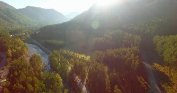 Vôo a meio do ar sobre o rio e o prado frescos da montanha na manhã ensolarada do verão. Estrada de terra rural abaixo. — Vídeo de Stock