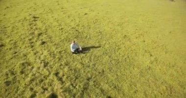 UHD 4k havadan görünümü. Defter pad ile yeşil çim sahasında oturan işadamı üzerinde düşük yörünge uçuş