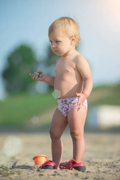 Niedliches Baby spielt mit Spielzeug am Sandstrand in Meeresnähe. — Stockfoto