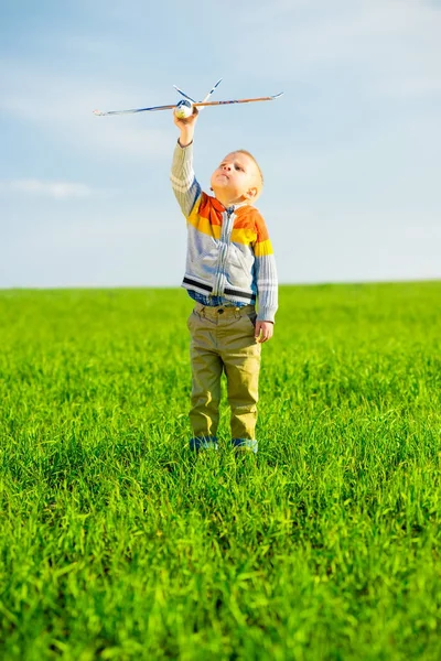 Счастливый мальчик играет с игрушечным самолетом на фоне голубого летнего неба и зеленого поля . — стоковое фото