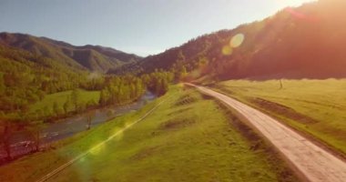 Güneşli yaz sabahında taze dağ nehri ve çayır üzerinde uçuşun ortasında. Aşağıdaki kırsal toprak yol.