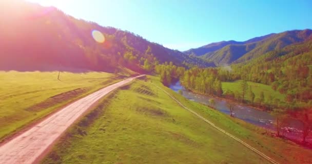 Közepes repülés a friss hegyi folyó és rét felett a napos nyári reggelen. Vidéki földút alatta. — Stock videók