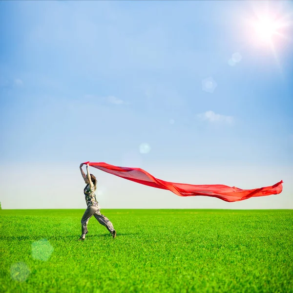 Beautiful young woman jumping on a green meadow with colored tissue — Stock Photo, Image