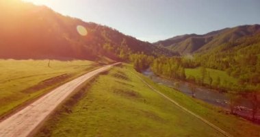Güneşli yaz sabahında taze dağ nehri ve çayır üzerinde uçuşun ortasında. Aşağıdaki kırsal toprak yol.