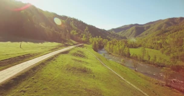 Volo a mezz'aria sul fiume fresco di montagna e prato al mattino d'estate soleggiato. Strada sterrata rurale sotto. — Video Stock