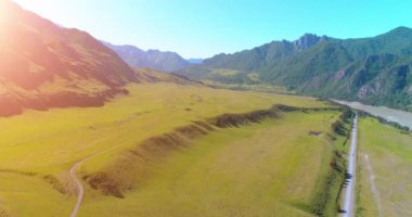 Güneşli yaz sabahında havadan kırsal dağ yolu ve çayır. Asfalt karayolu ve nehir.