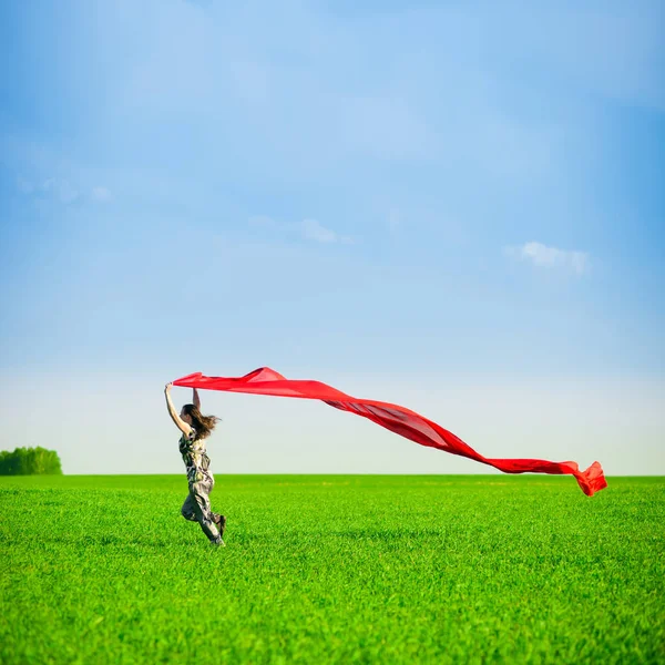 Belle jeune femme sautant sur une prairie verte avec des tissus colorés — Photo