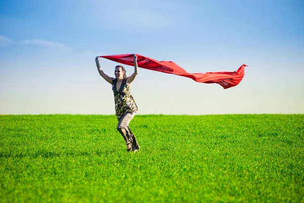 Beautiful young woman jumping on a green meadow with colored tissue — Stock Photo, Image