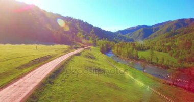 Güneşli yaz sabahında taze dağ nehri ve çayır üzerinde uçuşun ortasında. Aşağıdaki kırsal toprak yol.