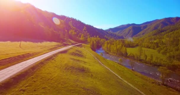 Mid air flight over fresh mountain river and meadow at sunny summer morning. Rural dirt road below. — Stock Video