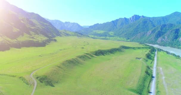 Aerial rural mountain road and meadow at sunny summer morning. Asphalt highway and river. — Stock Video