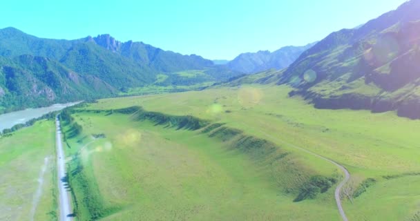 Aerial rural mountain road and meadow at sunny summer morning. Asphalt highway and river. — Stock Video