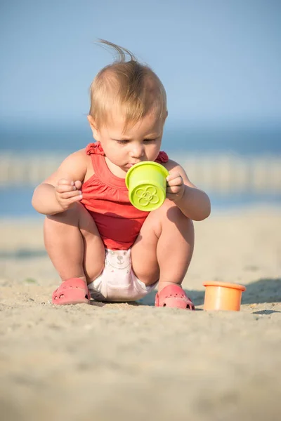 Bambina in abito rosso che gioca sulla spiaggia di sabbia vicino al mare . — Foto Stock