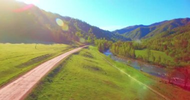 Güneşli yaz sabahında taze dağ nehri ve çayır üzerinde uçuşun ortasında. Aşağıdaki kırsal toprak yol.
