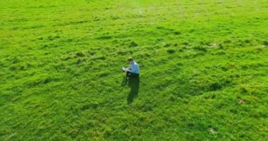UHD 4k havadan görünümü. Defter pad ile yeşil çim sahasında oturan işadamı üzerinde düşük yörünge uçuş